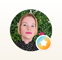 Femme blonde en chemisier à pois devant un mur végétal avec un badge étoilé.