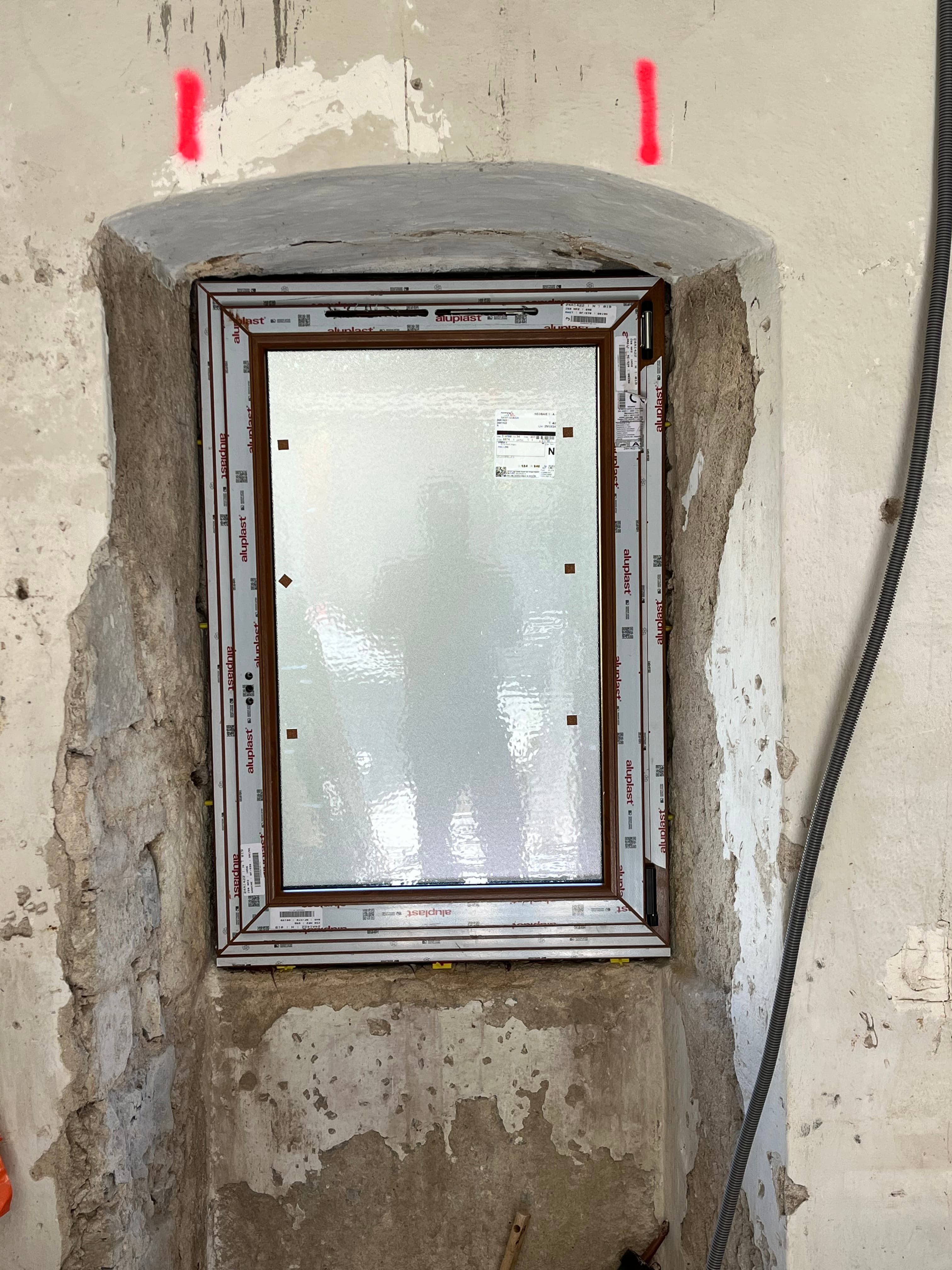 Fenêtre neuve avec cadre marron installée dans un mur en pierre brute en rénovation.