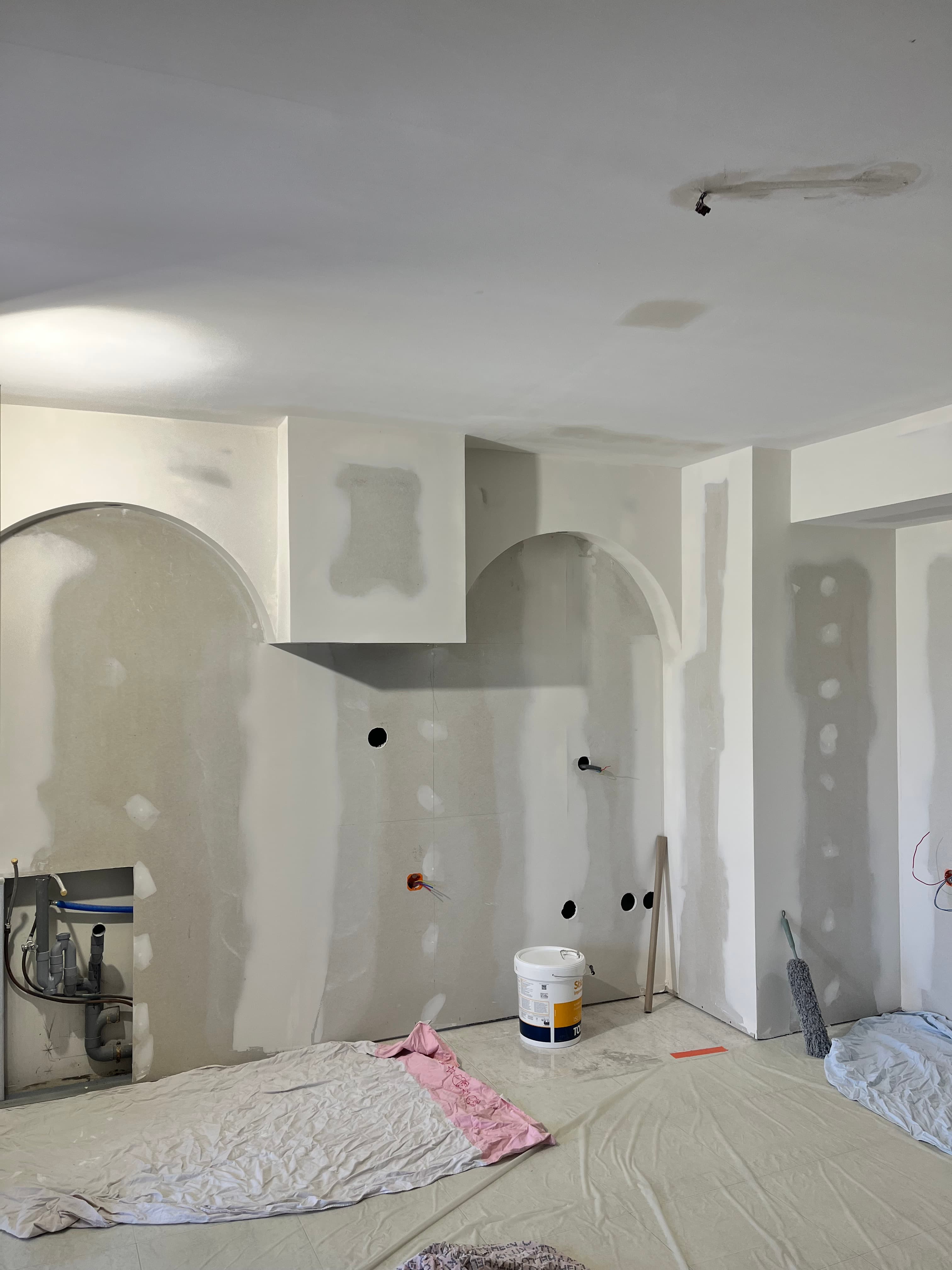 Intérieur en rénovation avec plaques de plâtre, arches intégrées, joints enduits et tuyauterie apparente.