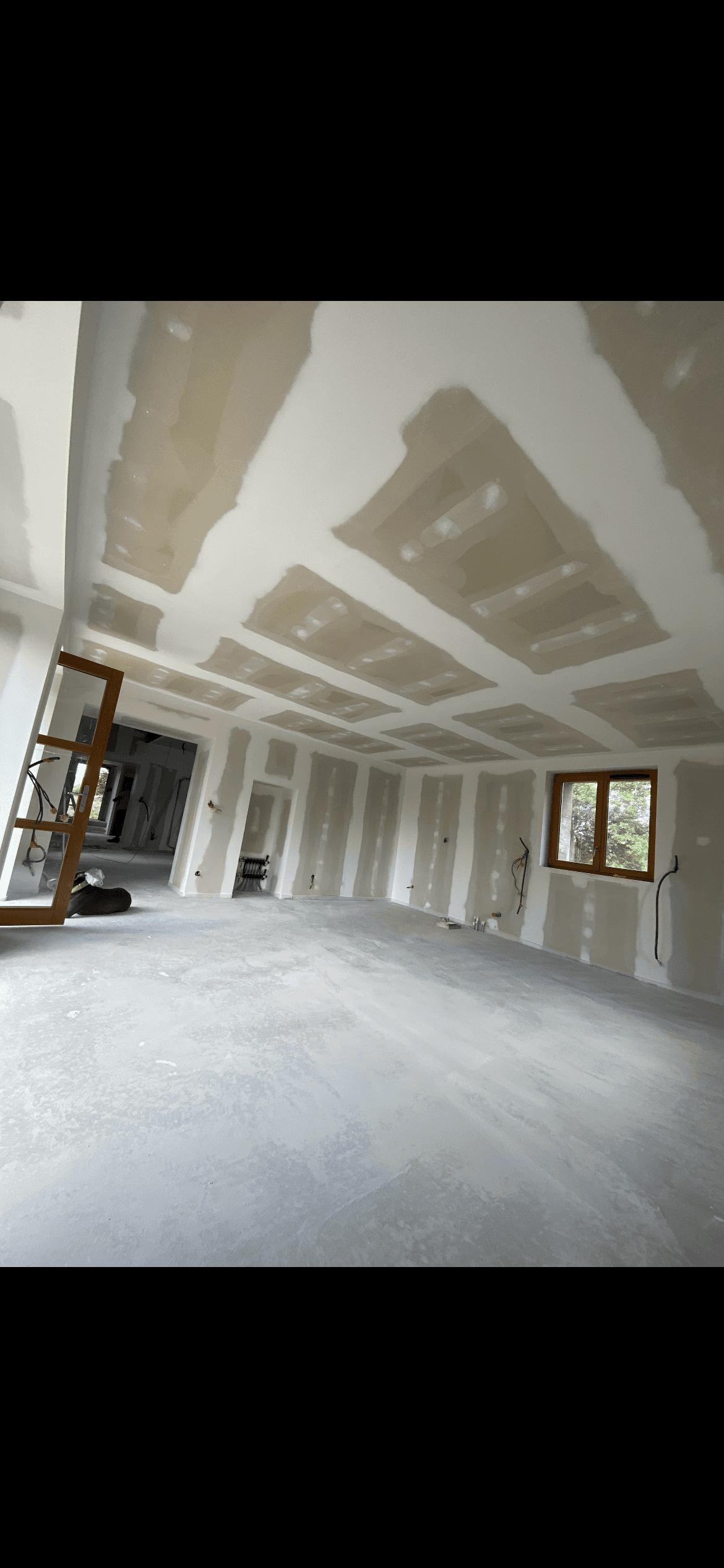 Intérieur d'une maison en chantier avec plaques de plâtre et enduit aux murs et plafond.