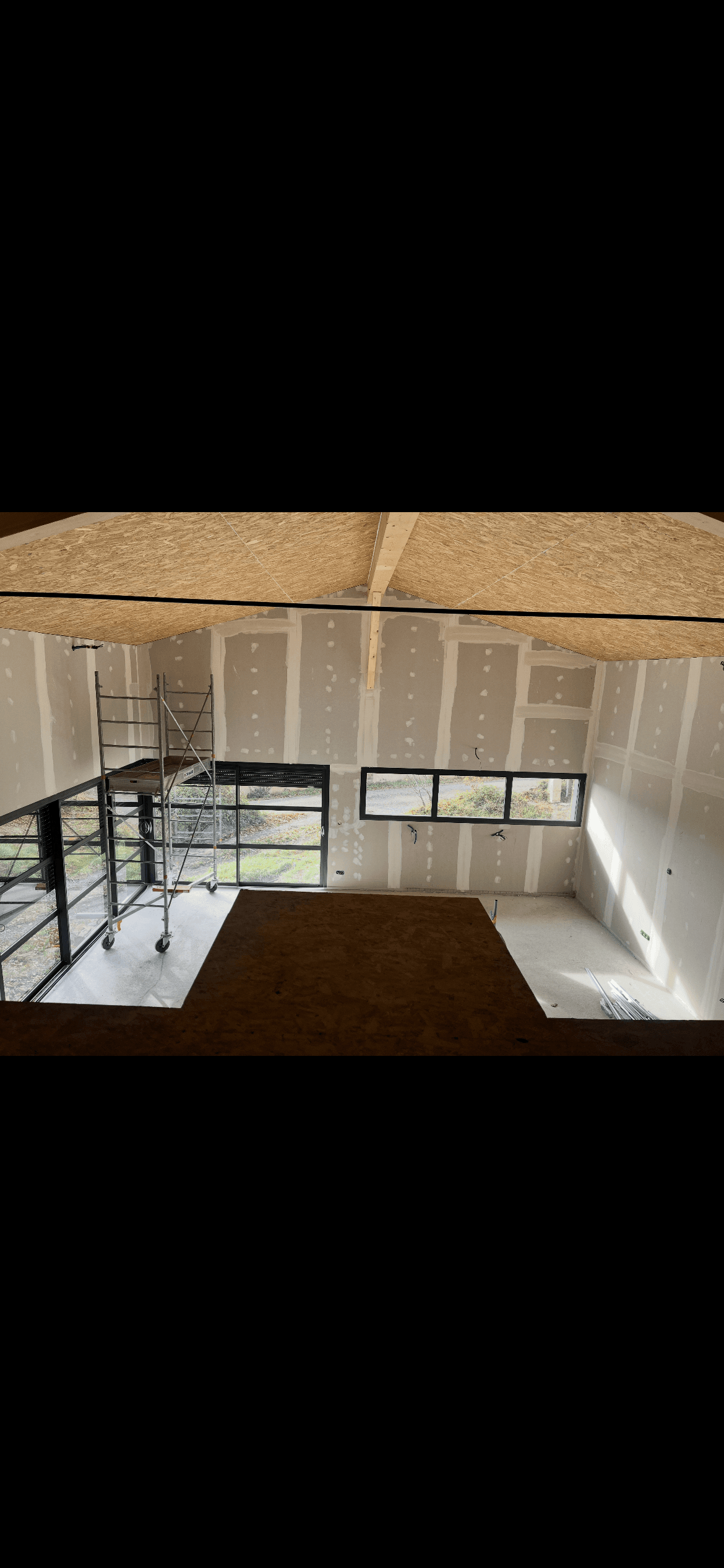 Chantier intérieur avec murs en plaques de plâtre, plafond OSB et échafaudage sur roulettes.