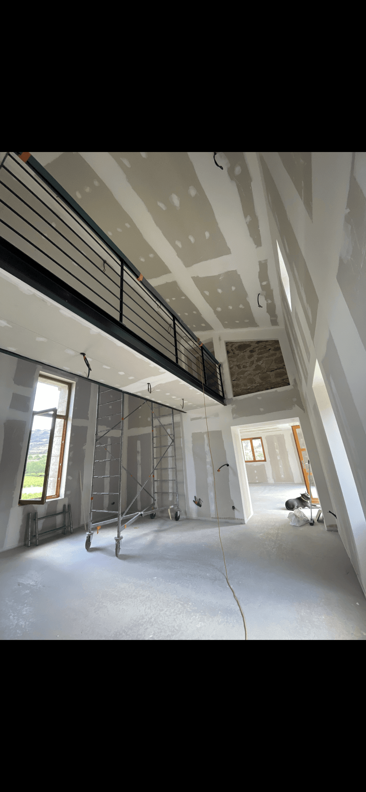 Intérieur en rénovation avec plaques de plâtre, mezzanine à garde-corps noir et échafaudage métallique.